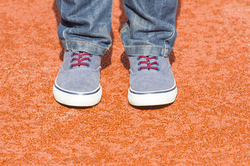 Boy in blue sneakers and jeans standing on red playground background. Close up leg's shot. Top view.