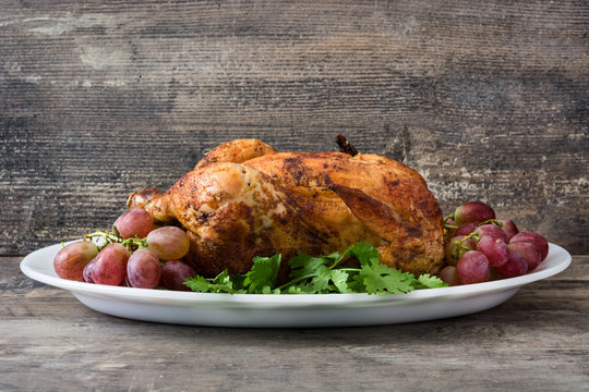 Garnished roasted turkey with grapes and herbs on a wooden table

