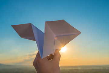 The hand hold paper airplane and launch by the bright sun and picturesque landscape background