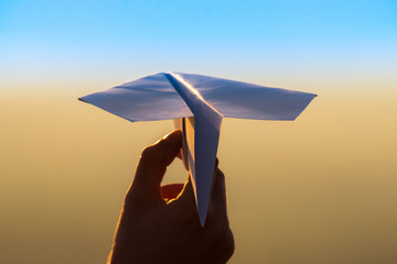 The hand hold paper airplane and launch on the background of picturesque sunset