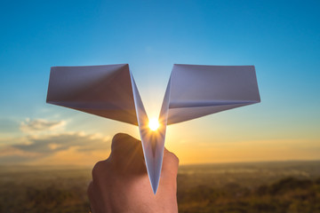 The hand hold paper airplane and launch on the background of bright sun and picturesque sunset