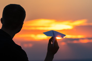 The man hold paper airplane and launch on the background of picturesque sunset