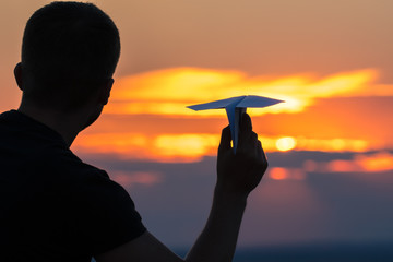 The man hold paper airplane and launch on the background of picturesque sunset