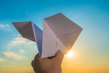 The hand hold paper airplane and launch on the background of bright sun and picturesque sunset