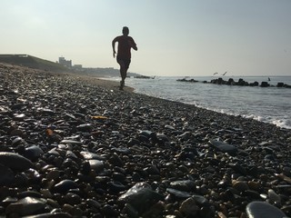 Backlit shot of man running on pebble beach