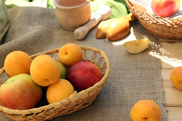 Apricots and apples in wattled basket on sackcloth on a wooden t