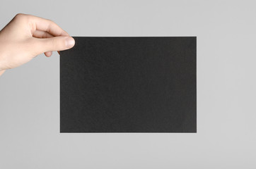 Black A5 Flyer / Invitation Mock-Up - Male hands holding a black flyer on a gray background.