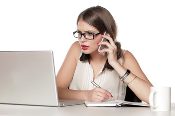 a young woman working on a laptop, talking on the phone and writes