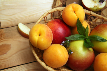 Apricots and apples in wattled basket on wooden table.