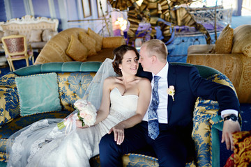 Fototapeta premium Wedding couple indoors is hugging each other. Beautiful model girl in white dress. Man in suit. Beauty bride with groom. Female and male portrait. Woman with lace veil. Cute lady and handsome guy
