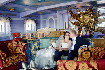 Wedding couple indoors is hugging each other. Beautiful model girl in white dress. Man in suit. Beauty bride with groom. Female and male portrait. Woman with lace veil. Cute lady and handsome guy