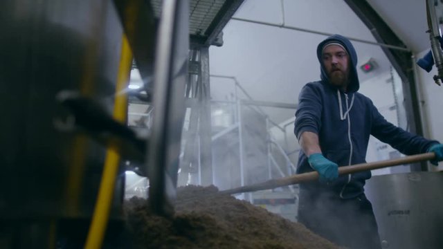  Worker in a brewery removing mash from the bottom of a machine