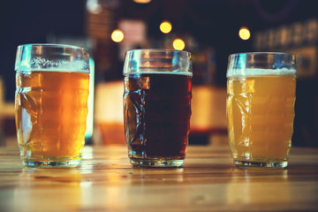 Beautiful background of the Oktoberfest. Glasses of cold fresh white, light and dark beer on the wooden bar counter in the pub. Assorted alcohol in a Flight Ready for Tasting