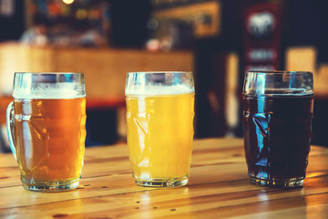 Beautiful background of the Oktoberfest. Glasses of cold fresh white, light and dark beer on the wooden bar counter in the pub. Assorted alcohol in a Flight Ready for Tasting