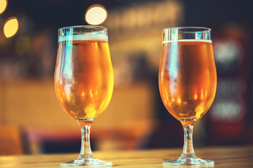 Two glasses of fresh cold light beer on a wooden bar counter in pub with free space for your text. Beautiful background of the Oktoberfest.
