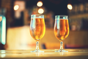 Two glasses of fresh cold light beer on a wooden bar counter in pub with free space for your text. Beautiful background of the Oktoberfest.