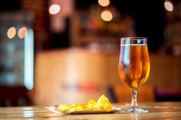 A fresh glass of cold light beer and potato chips on the wooden bar counter in pub with free space...