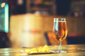 Fototapeta premium A fresh glass of cold light beer and potato chips on the wooden bar counter in pub with free space for your text. Beautiful background of the Oktoberfest.