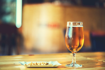 A fresh glass of cold light beer and salty peanut on the wooden bar counter in pub with free space for your text. Beautiful background of the Oktoberfest.
