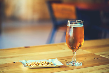 A fresh glass of cold light beer and salty peanut on the wooden bar counter in pub with free space for your text. Beautiful background of the Oktoberfest.