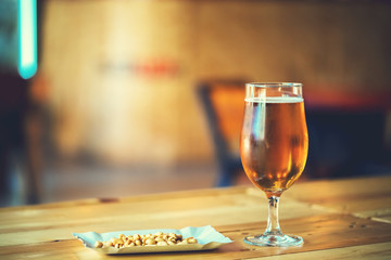 A fresh glass of cold light beer and salty peanut on the wooden bar counter in pub with free space for your text. Beautiful background of the Oktoberfest.