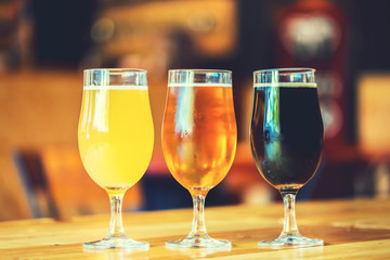 Beautiful background of the Oktoberfest. Glasses of cold fresh white, light and dark beer on the wooden bar counter in the pub. Assorted alcohol in a Flight Ready for Tasting