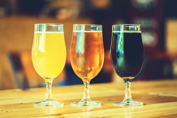 Beautiful background of the Oktoberfest. Glasses of cold fresh white, light and dark beer on the wooden bar counter in the pub. Assorted alcohol in a Flight Ready for Tasting