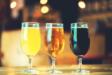 Beautiful background of the Oktoberfest. Glasses of cold fresh white, light and dark beer on the wooden bar counter in the pub. Assorted alcohol in a Flight Ready for Tasting