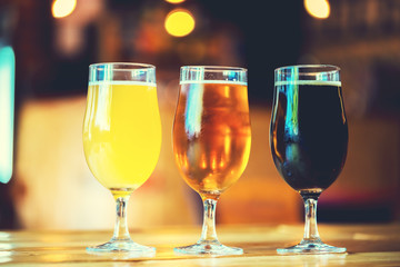 Beautiful background of the Oktoberfest. Glasses of cold fresh white, light and dark beer on the wooden bar counter in the pub. Assorted alcohol in a Flight Ready for Tasting