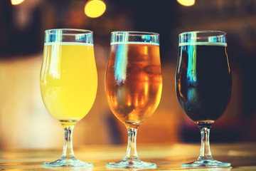 Glasses of cold fresh white, light and dark beer on the wooden bar counter in the pub. Assorted alcohol in a Flight Ready for Tasting. fine grain. Soft focus. Shallow DOF