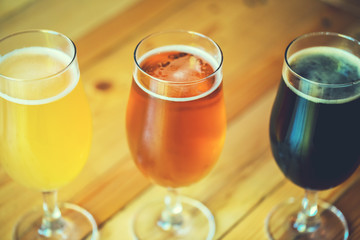 Beautiful background of the Oktoberfest. Glasses of cold fresh white, light and dark beer on the wooden bar counter in the pub. Assorted alcohol in a Flight Ready for Tasting