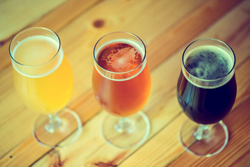 Beautiful background of the Oktoberfest. Glasses of cold fresh white, light and dark beer on the wooden bar counter in the pub. Assorted alcohol in a Flight Ready for Tasting