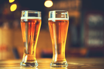 Two glasses of fresh cold light beer on a wooden bar counter in pub with free space for your text. Beautiful background of the Oktoberfest. fine grain. Soft focus. Shallow DOF
