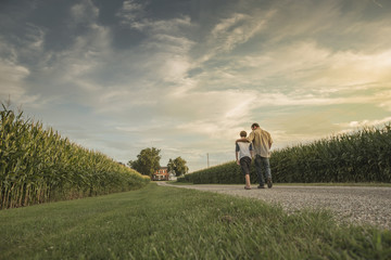Caucasian father and son walking on dirt path by corn field