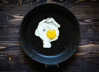 Fried egg in a black pan over a dark old dirty wood background
