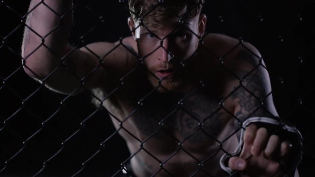  Muscular MMA fighter holding on to the fencing of the cage