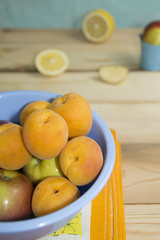 Apricots and apples in blue plastic bowl on wooden table.