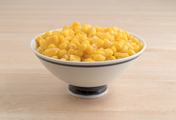 Organic sweet corn in a small bowl on a wood table.