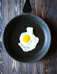 Fried egg in a black pan over a dark old dirty wood background