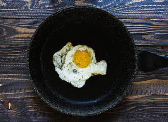 Fried egg in a black pan over a dark old dirty wood background