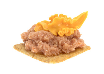 Deviled ham with canned cheese on a cracker against a white background.