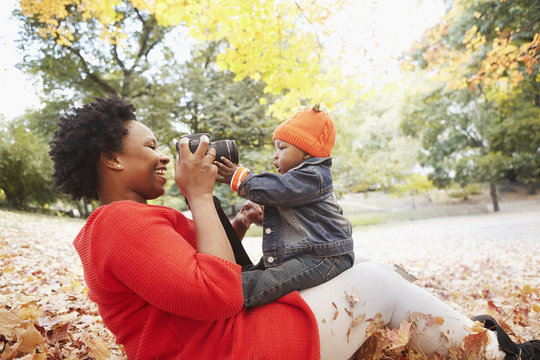 Black mother taking pictures of toddler son in park
