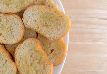 Crostini dabbed with olive oil on a plate atop a wood table.