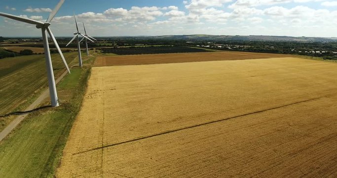 Aerial view looking across three wind turbines in motion on a summers day over wheat crops with a large open sky