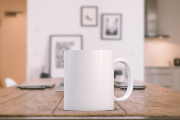 White blank coffee mug on a kitchen table with laptops in the background, ready for your custom...