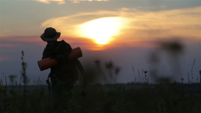 A tourist with a backpack and a camera at sunset in the field.
