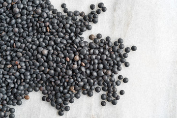 Black beluga lentils spilled on a marble counter top.