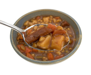 Spoonful of beef stew over bowl on a white background. 