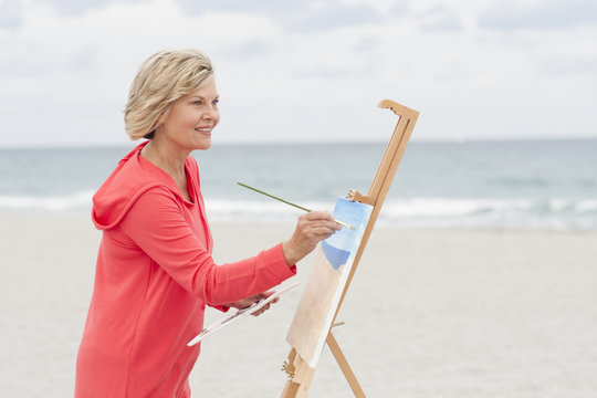 Older Caucasian woman painting on beach
