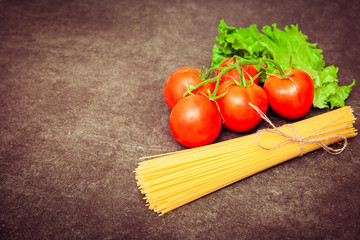 green onions, tomatoes, sweet pepper, and ceramic knife lying on the wooden circle board . Background dark wooden table. Virw from above. Copy space at left.